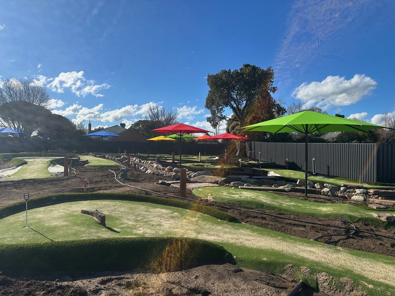 Sunny mini golf course with colourful umbrellas and a fenced seating area under a blue sky — The Gazebo and Shade Centre in Yarrawonga, VIC