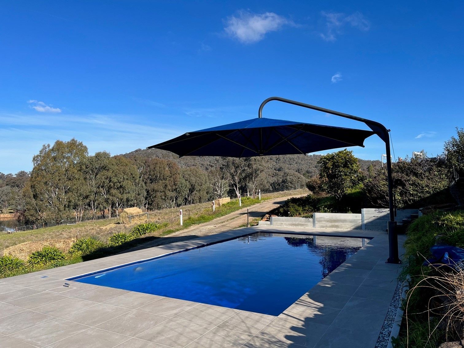 Backyard swimming pool with blue water and black shade sail under a clear blue sky — The Gazebo and Shade Centre in Jindera, NSW