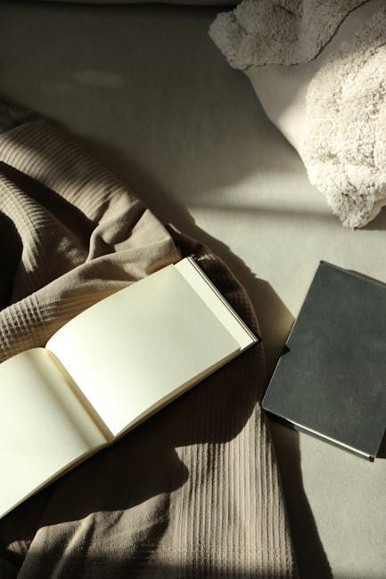 Een open, leeg notitieboek en een gesloten, zwart notitieboek liggen op een verfrommelde beige stoffen ondergrond in het warme zonlicht.