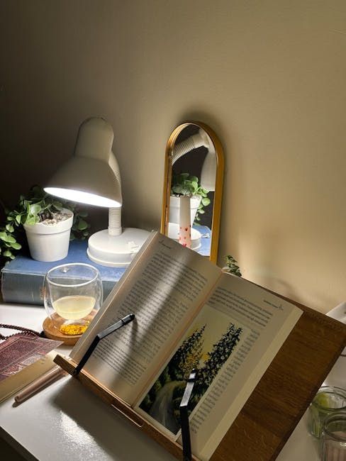 Bureau met een open boek onder een lamp, pen, thee en een spiegel naast een potplant.