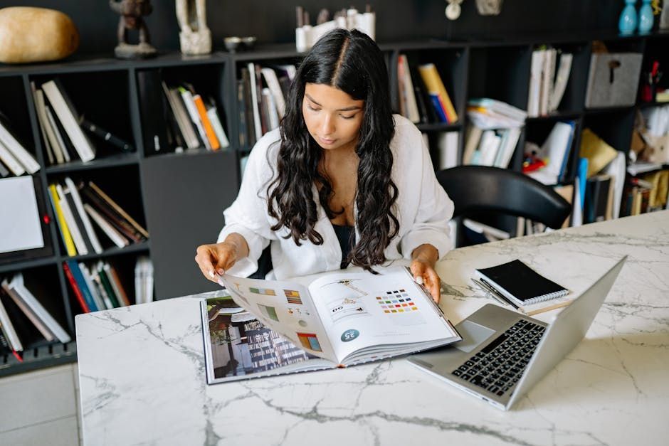 Iemand die een tijdschrift doorneemt aan een bureau met een laptop in een thuiskantoor.