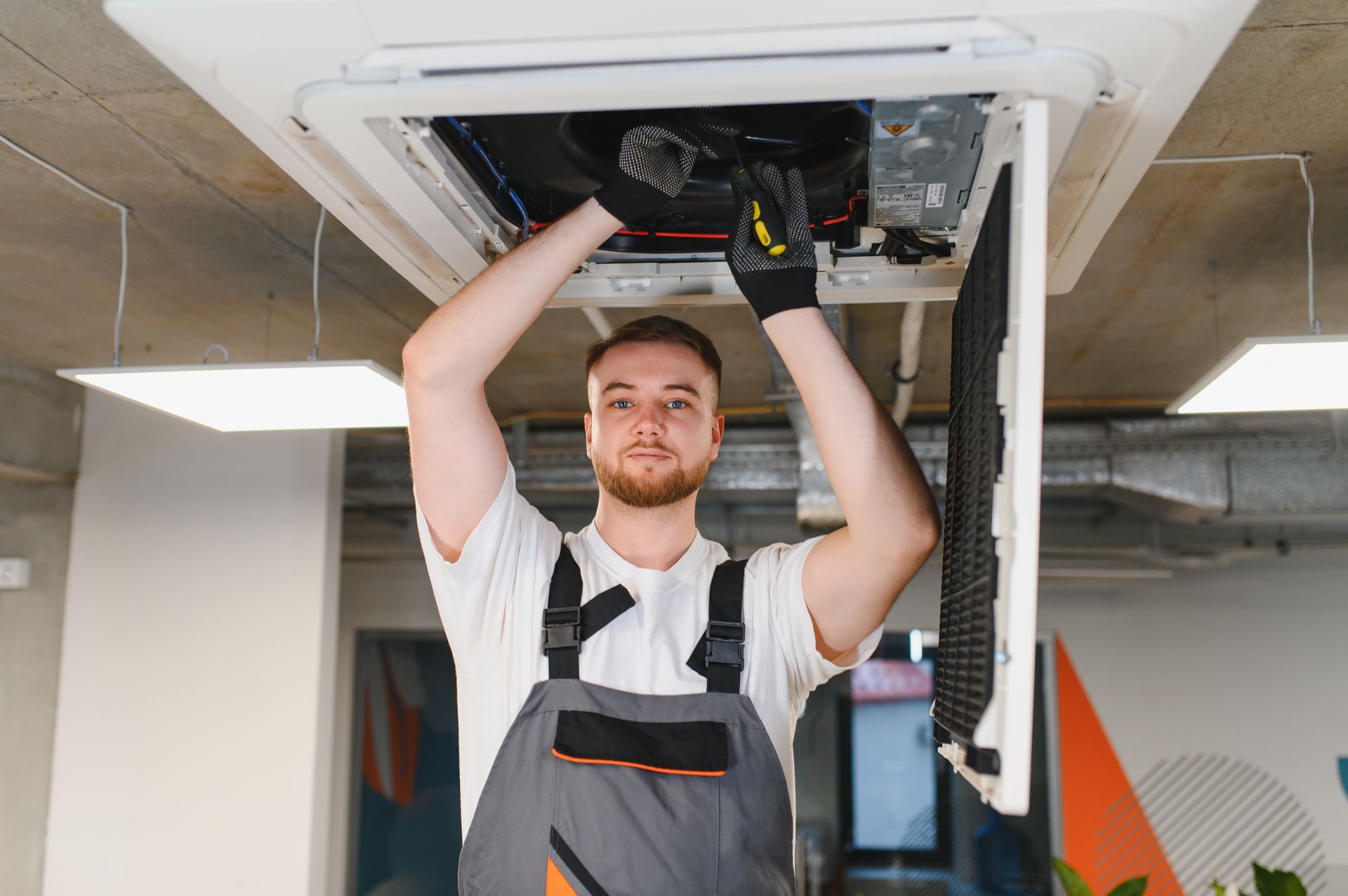 HVAC technician repairing ceiling air conditioning unit.
