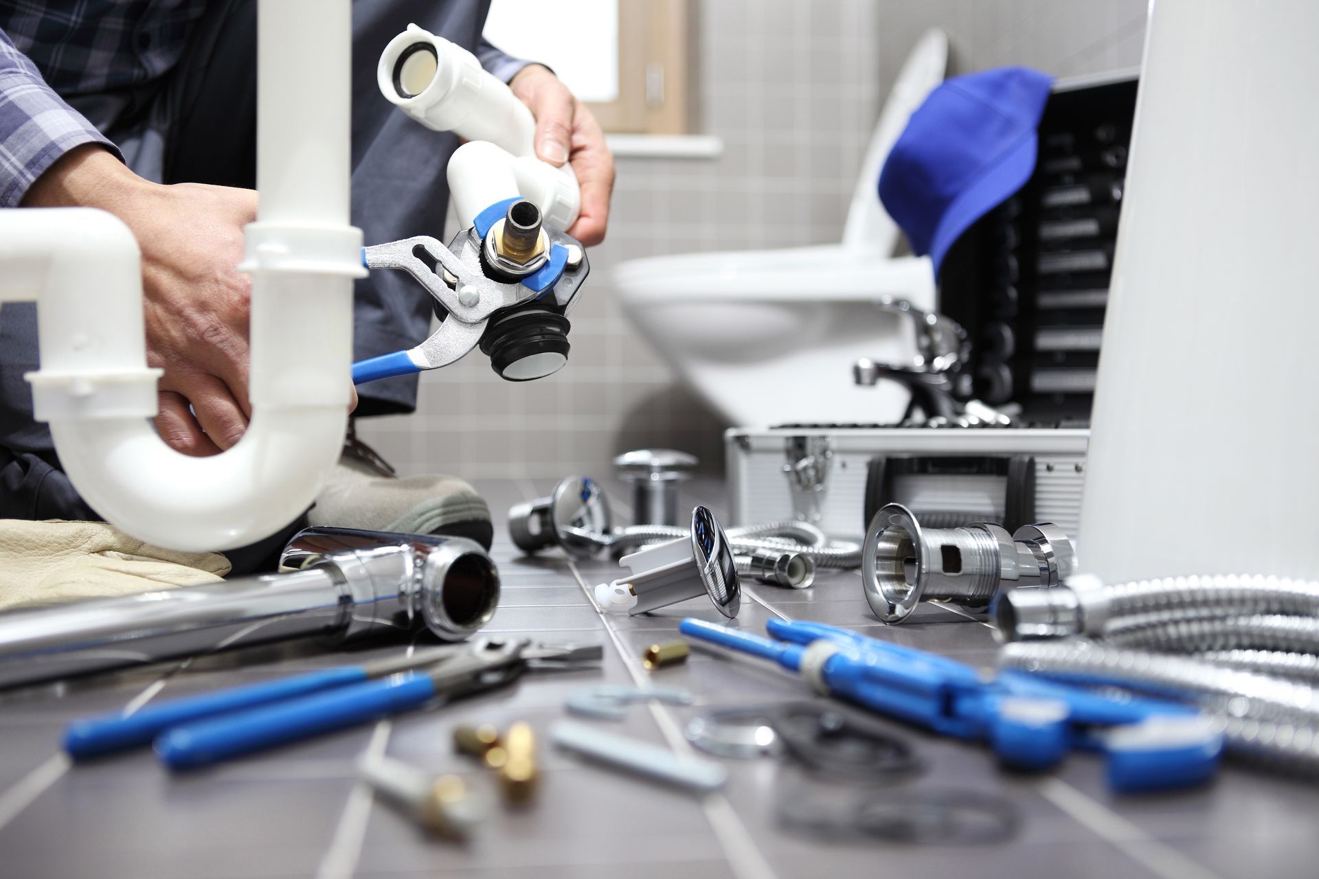 A plumber repairing bathroom sink pipes with a wrench, tools scattered on the tiled floor.
