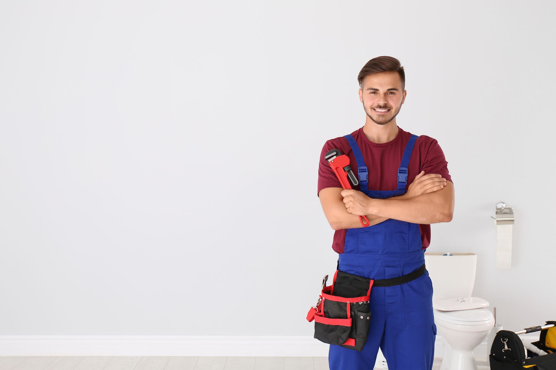 Young man with plumber wrench and toilet bowl on background. 