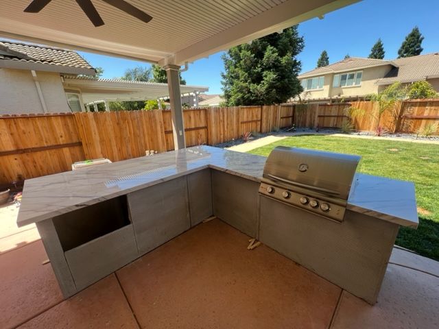 Outdoor kitchen with a built-in grill, counter, and storage under a patio cover.