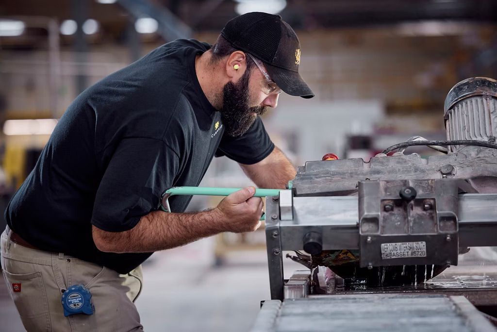 Man in black shirt and hat using a saw, focused, in a factory setting.