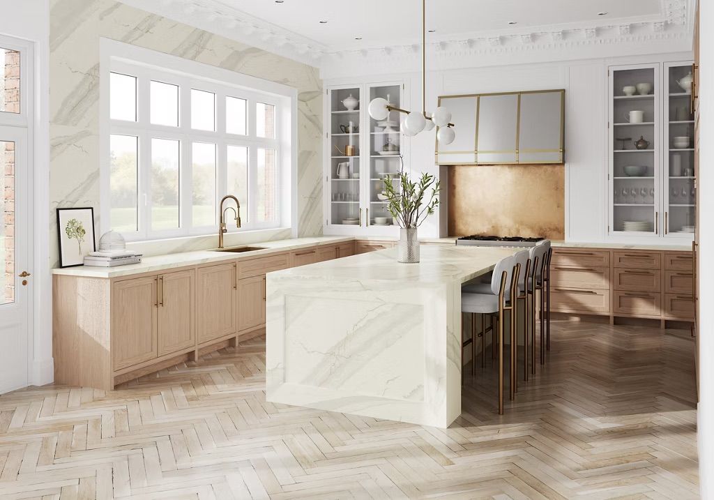 Elegant kitchen with light wood cabinets, marble countertops, and herringbone floors.