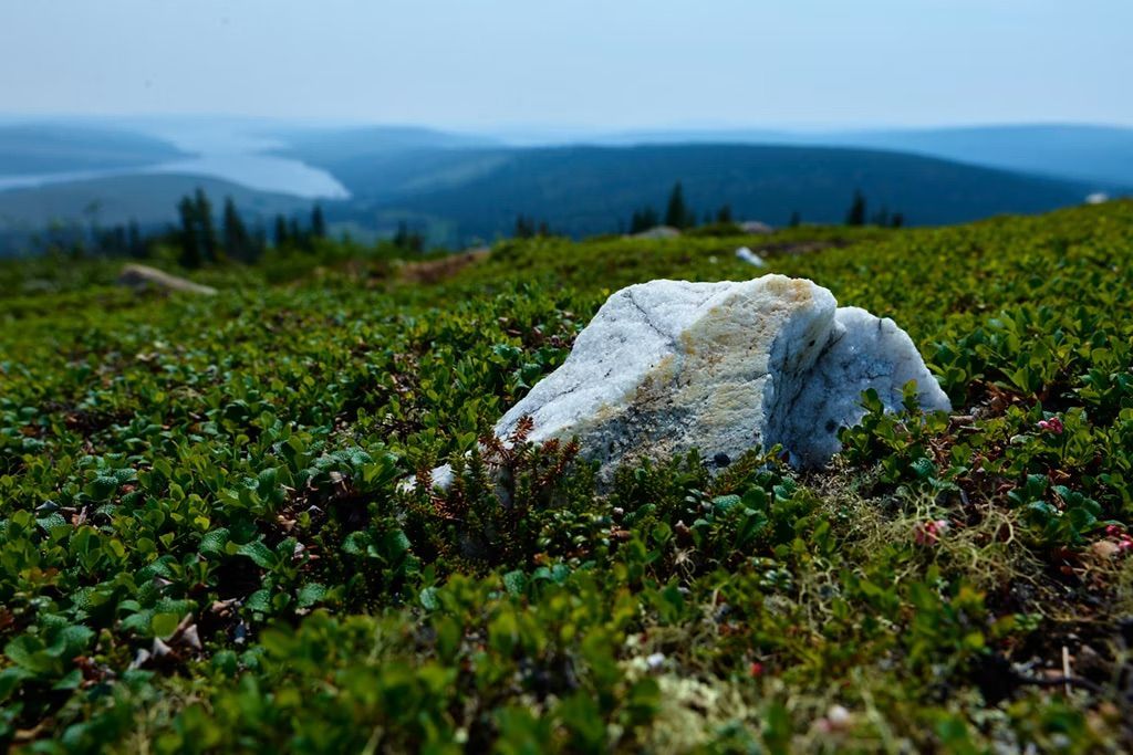 White rock on green ground, mountains and water in the distance, sunny landscape.