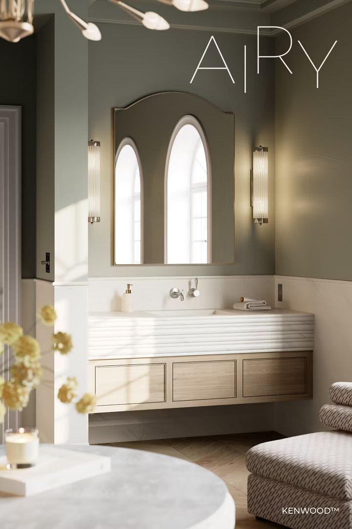 Bathroom with arched mirror, light wood vanity, sage green walls, and a marble-topped round table.