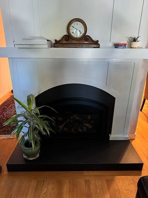 White fireplace with black interior, shelf displays clock and plant.