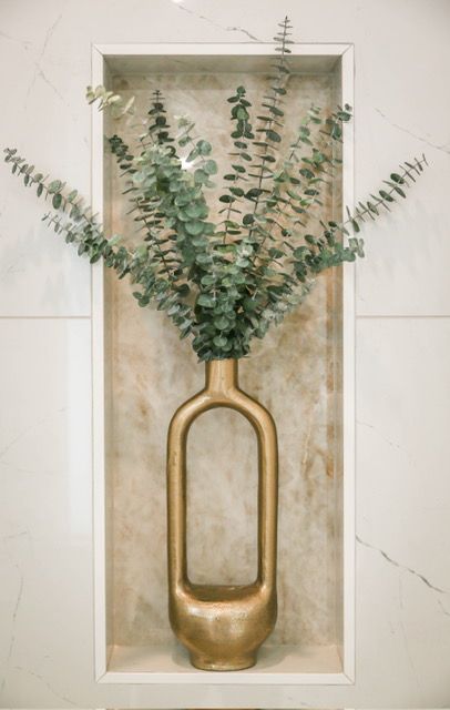 Gold vase with eucalyptus branches in a wall niche with a marble-like background.