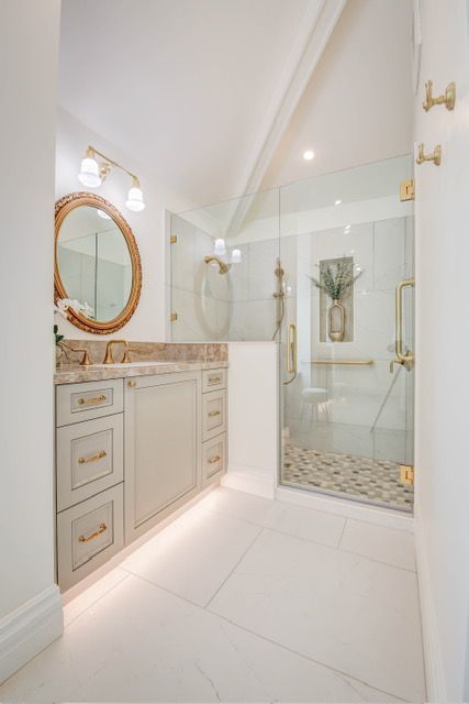 Elegant, bright bathroom with a glass shower, vanity, and gold accents.