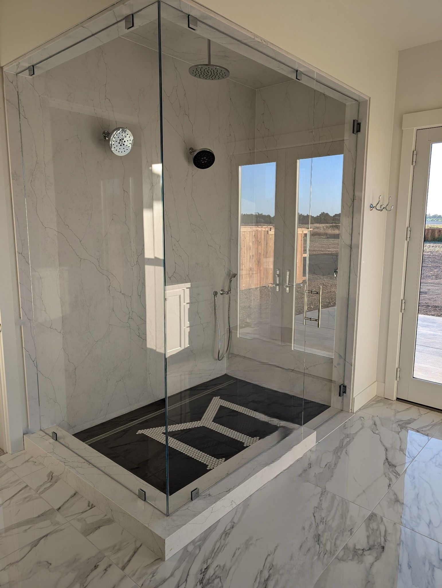 Glass shower enclosure with black and white tile floor and chrome fixtures.