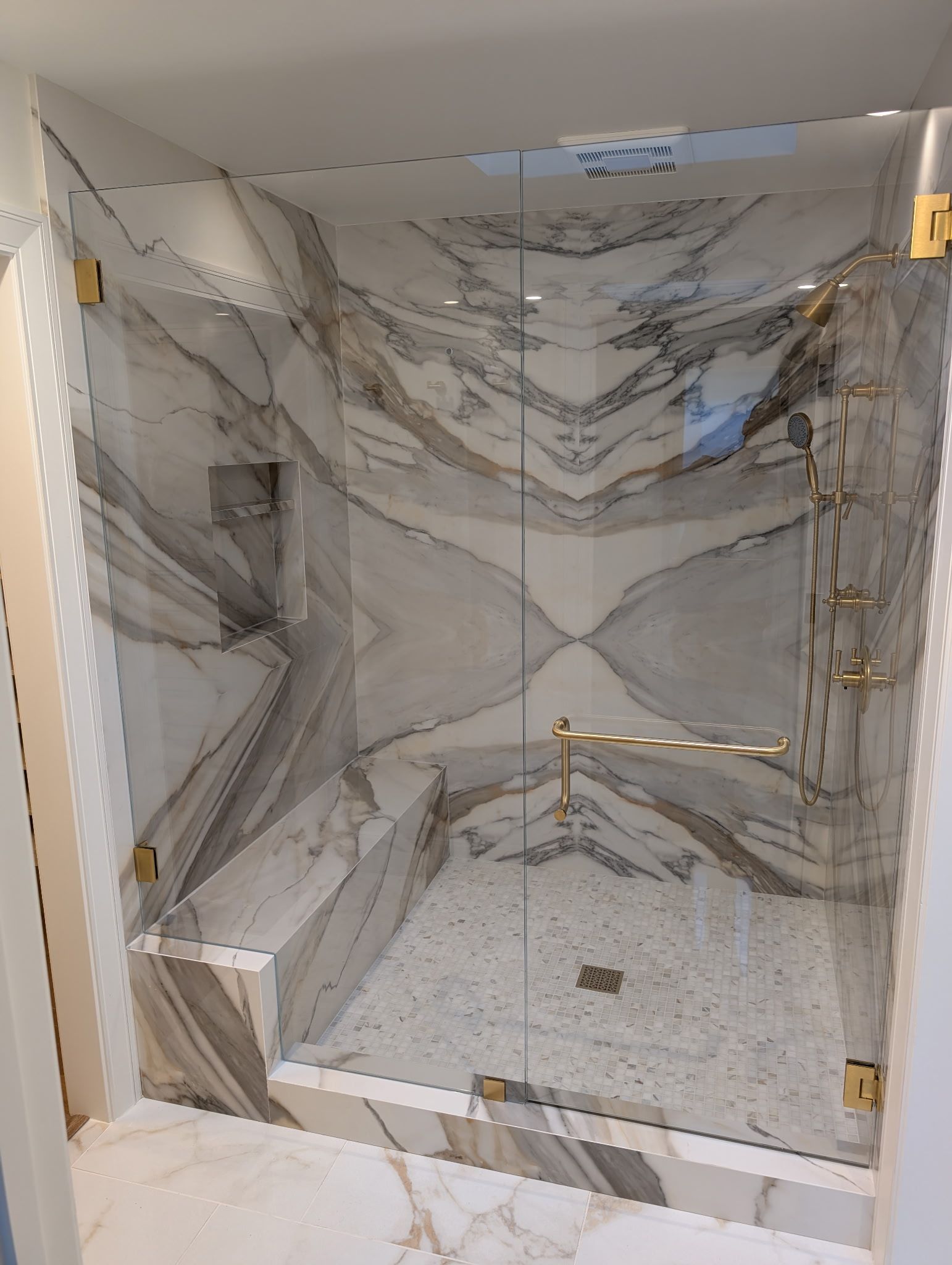 Glass-enclosed shower with gold hardware and marble walls and floor.