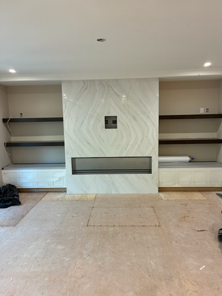 Fireplace with built-in shelves and marble accent wall. Shelves are dark. Unfinished flooring.