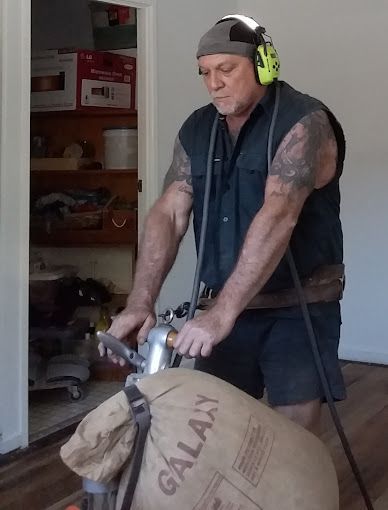 A Man Is Sanding A Wooden Floor With A Machine — Dale Dow Floor Sanding In Kirwan, QLD