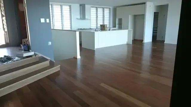 A Large Empty Room With Hardwood Floors And Stairs Leading To A Kitchen — Dale Dow Floor Sanding In Kirwan, QLD