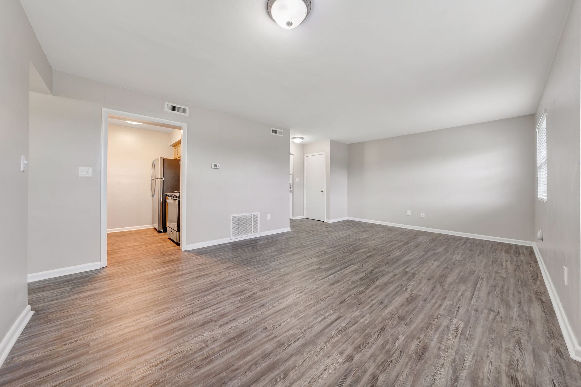 An empty living room with hardwood floors and a refrigerator.