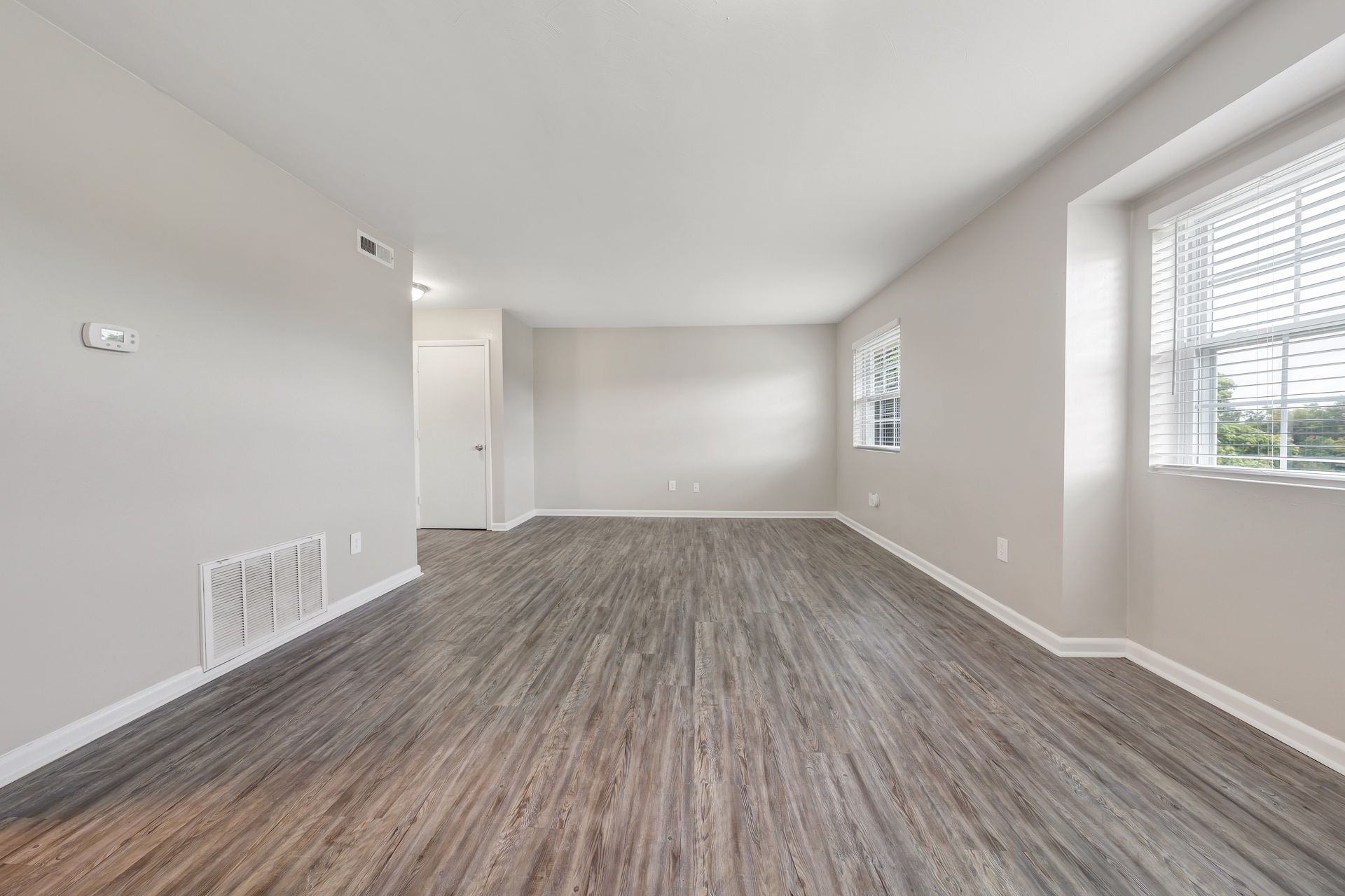 An empty living room with hardwood floors and two windows.