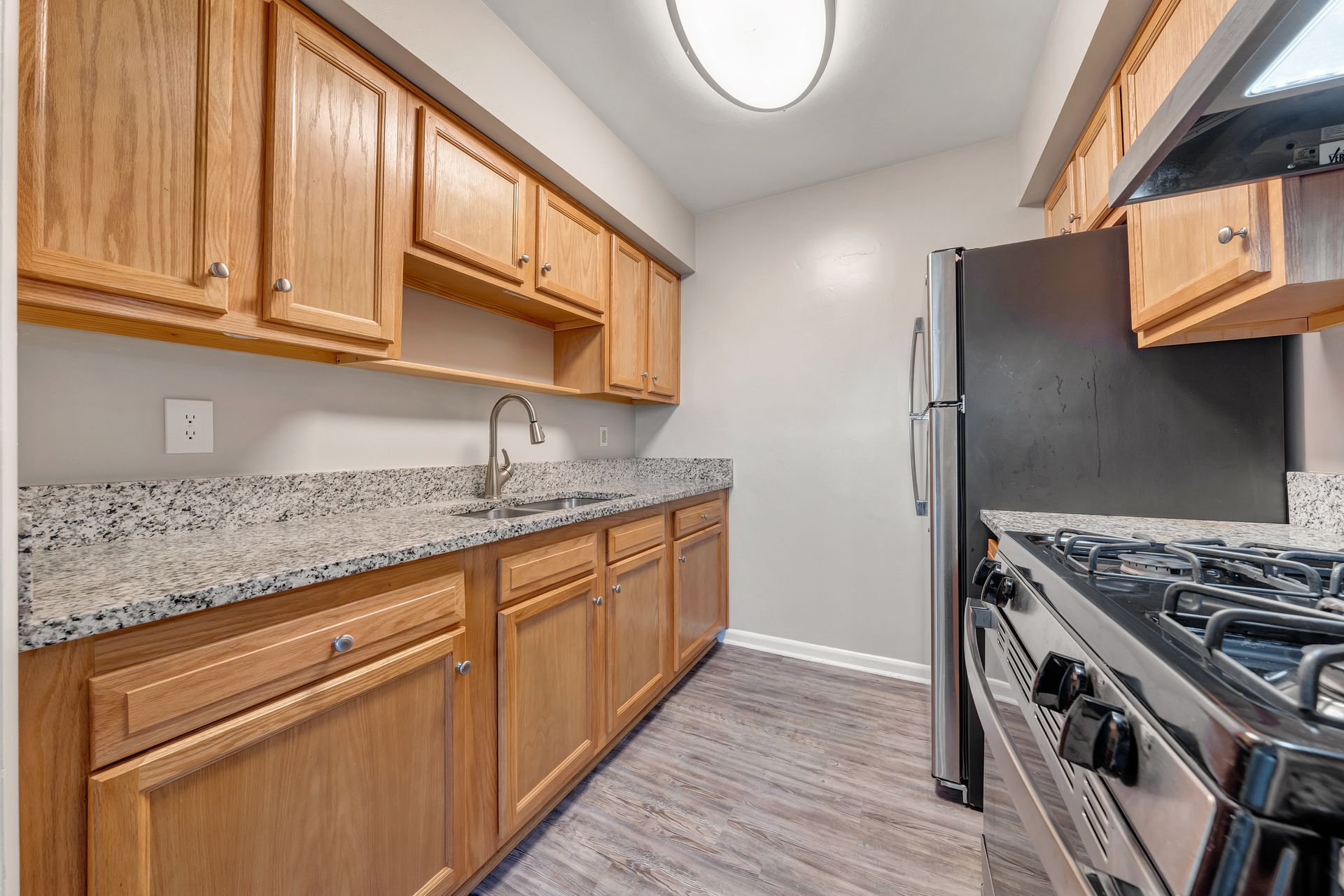 A kitchen with wooden cabinets , granite counter tops , a stove and a refrigerator.