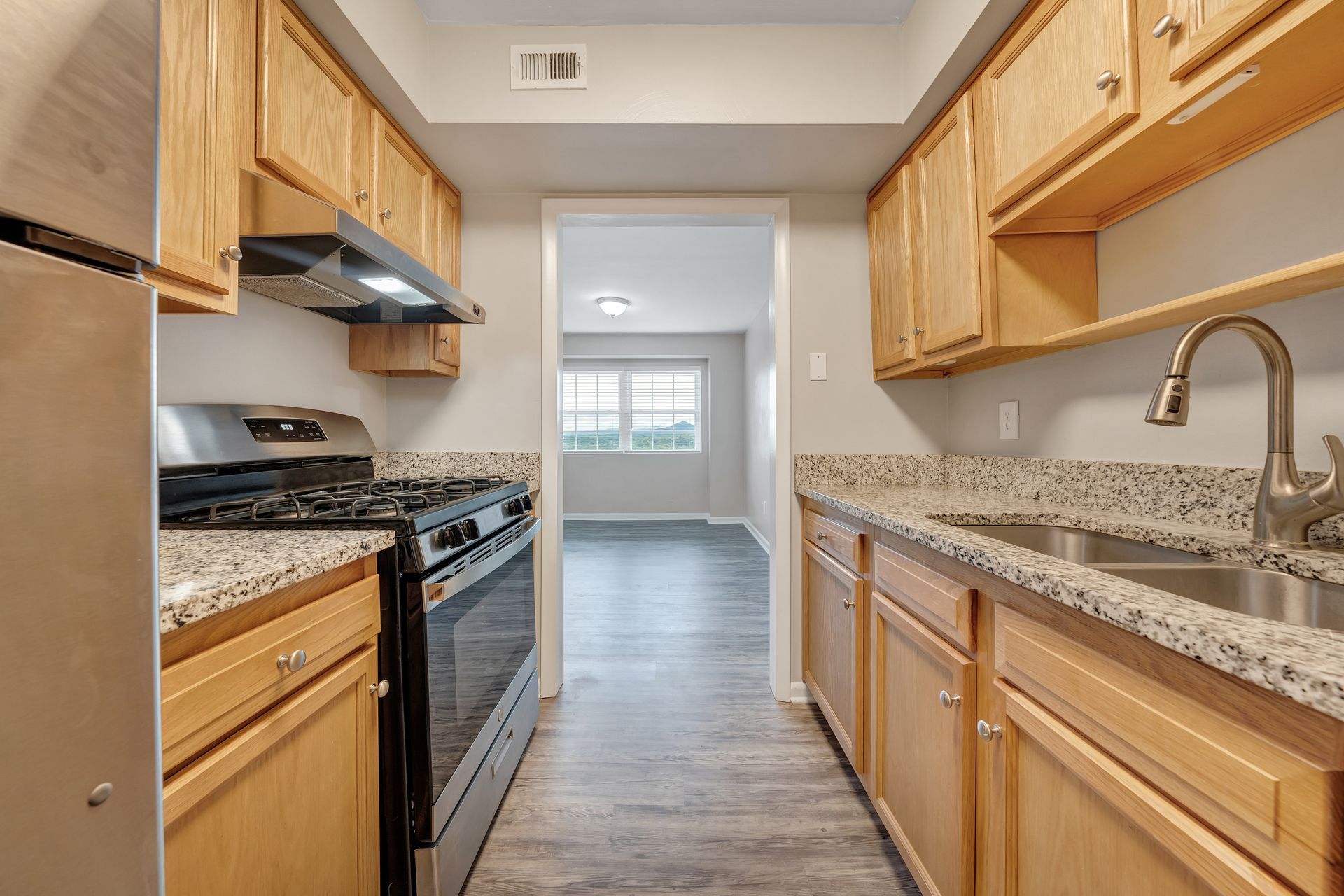 A kitchen with stainless steel appliances , granite counter tops , wooden cabinets and a sink.
