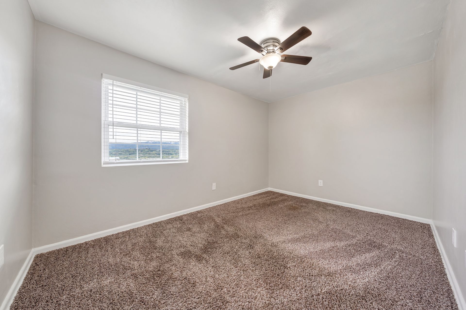 An empty bedroom with a ceiling fan and a window.