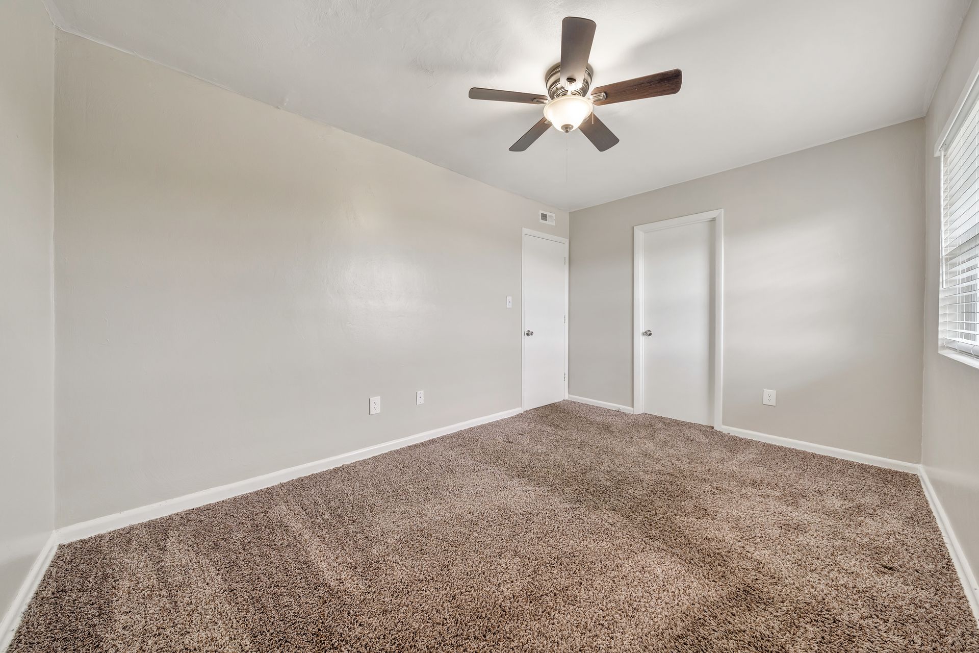 An empty bedroom with a ceiling fan and a window.
