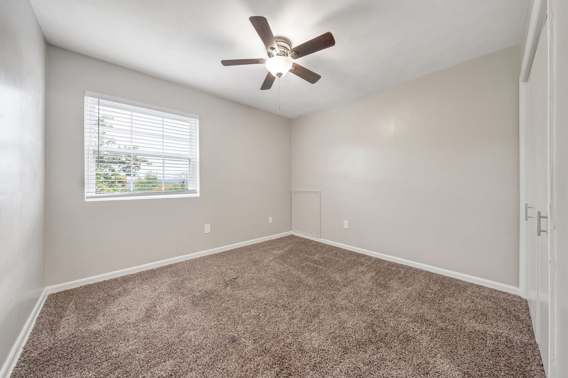 An empty bedroom with a ceiling fan and a window.