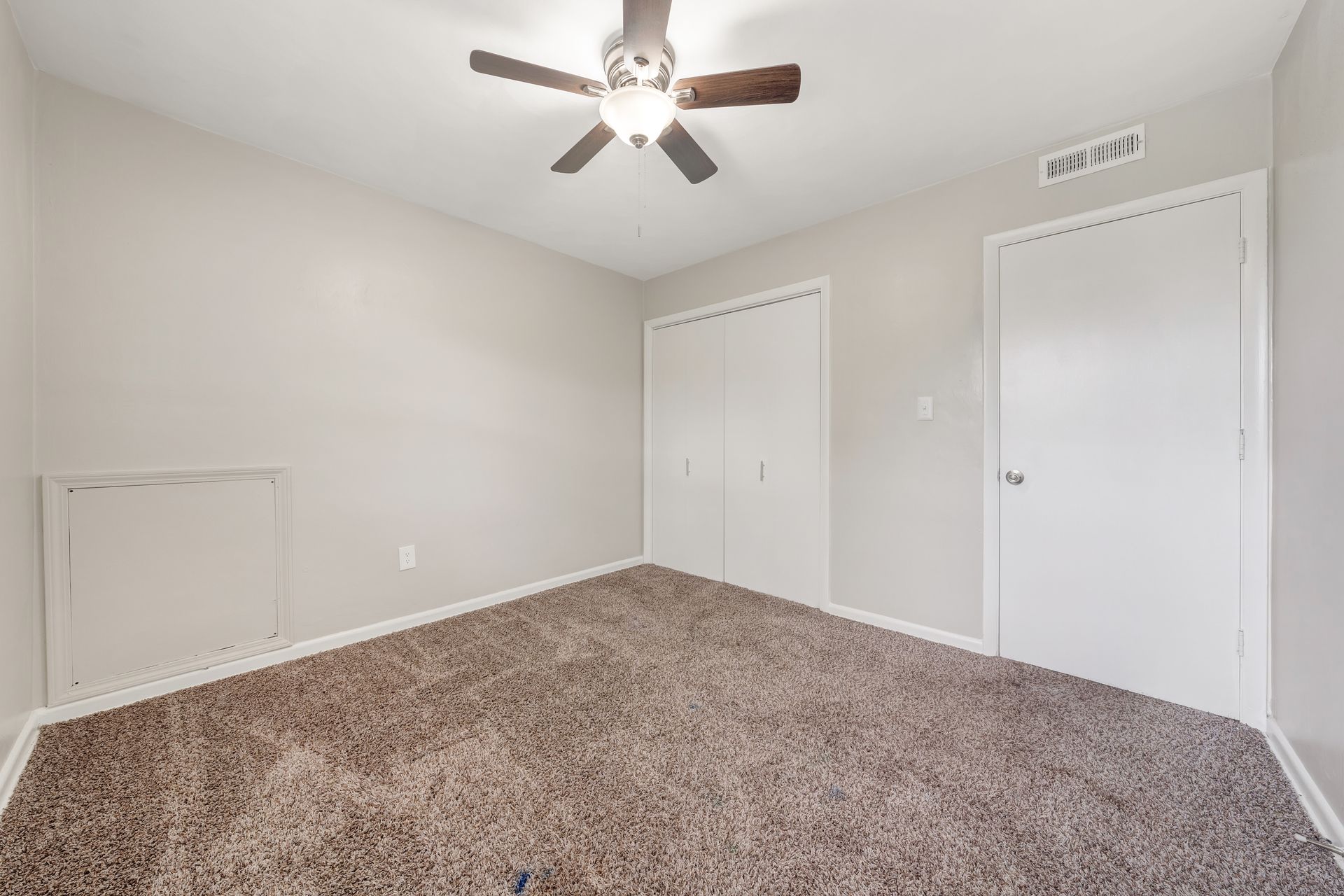 An empty bedroom with a ceiling fan and a carpeted floor.