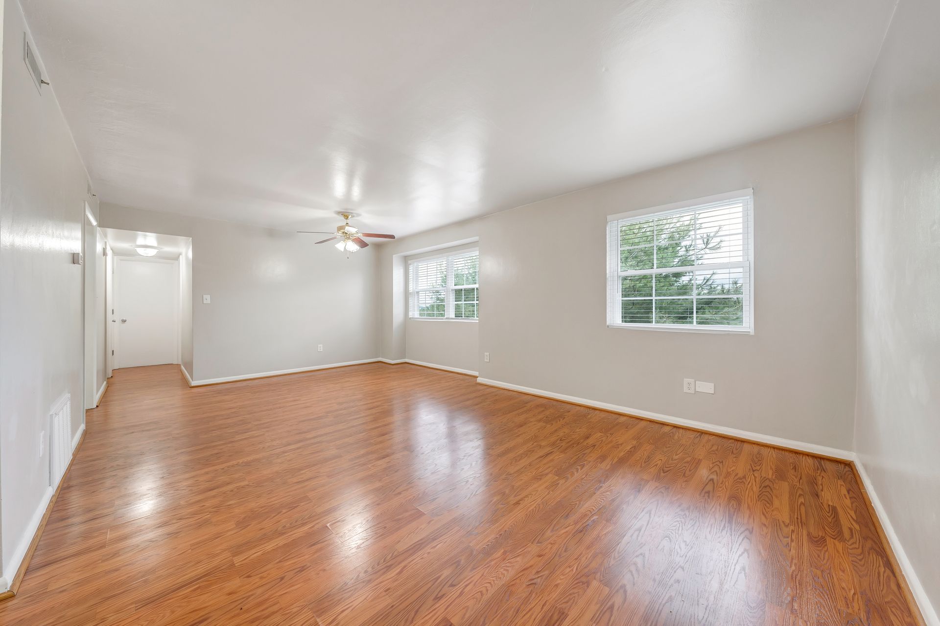 An empty living room with hardwood floors and a ceiling fan.