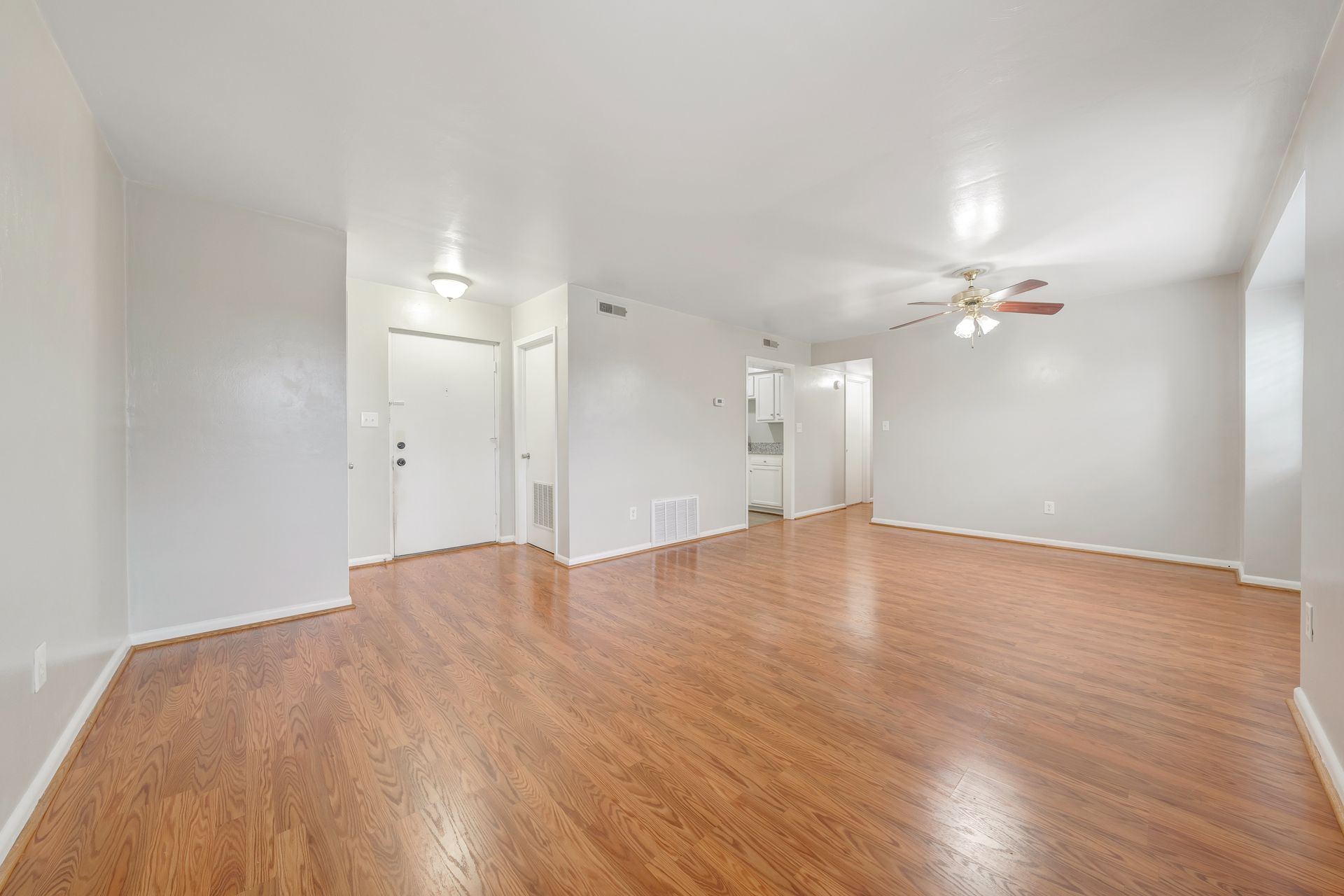 An empty living room with hardwood floors and a ceiling fan.