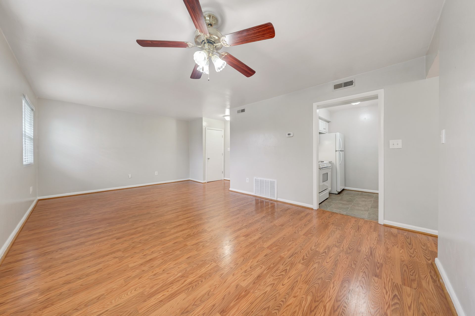 An empty living room with hardwood floors and a ceiling fan.