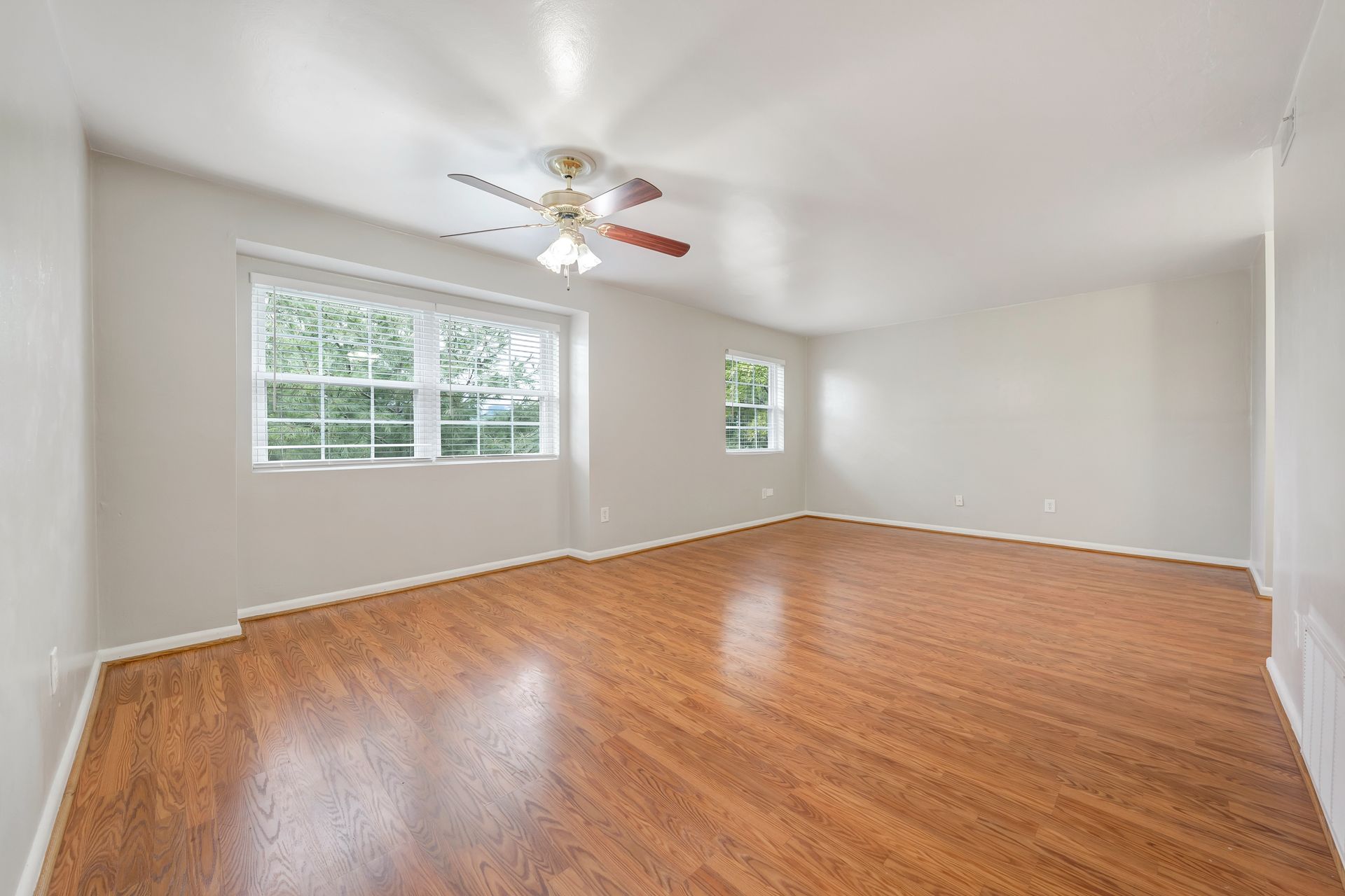 An empty living room with hardwood floors and a ceiling fan.