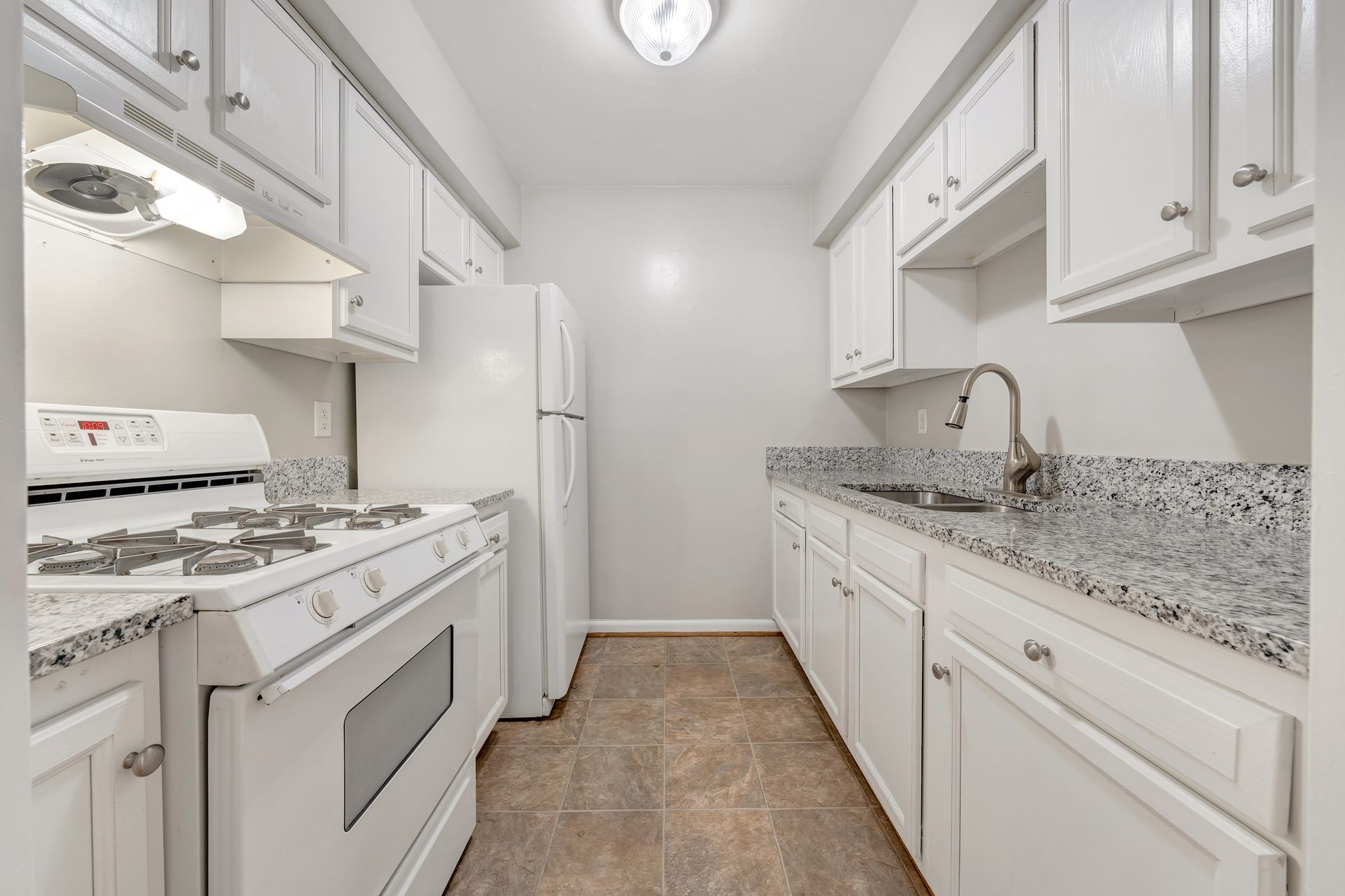 A kitchen with white cabinets , a stove , a refrigerator , and a sink.