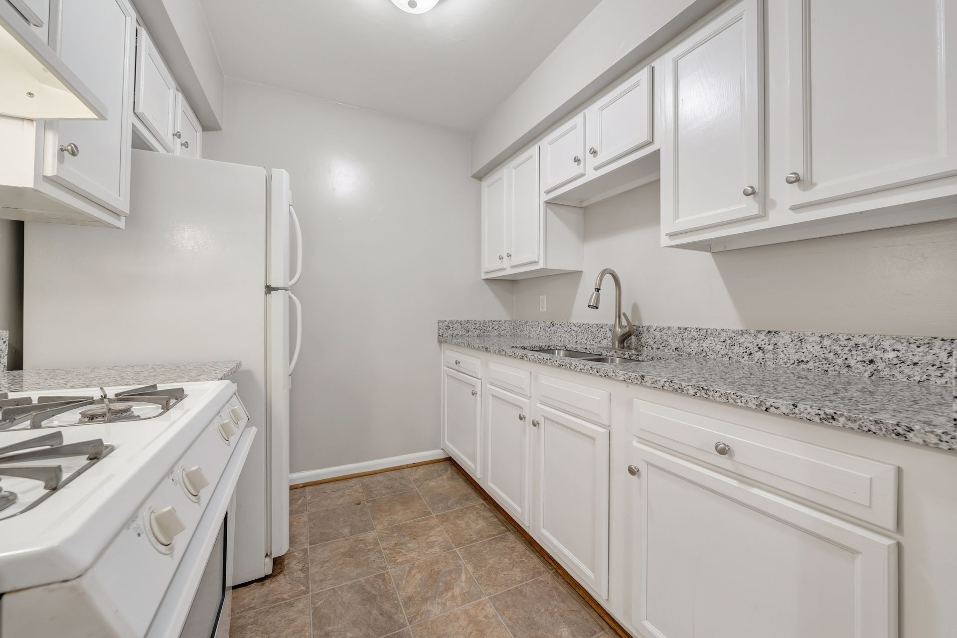 A kitchen with white cabinets , a refrigerator , a stove , and a sink.