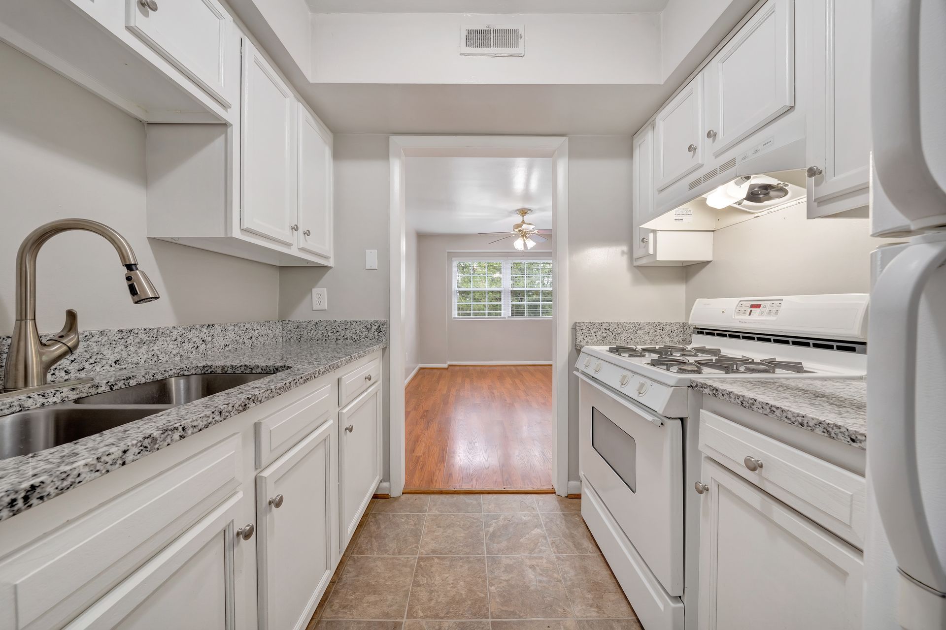 A kitchen with white cabinets , a stove , a sink and a refrigerator.