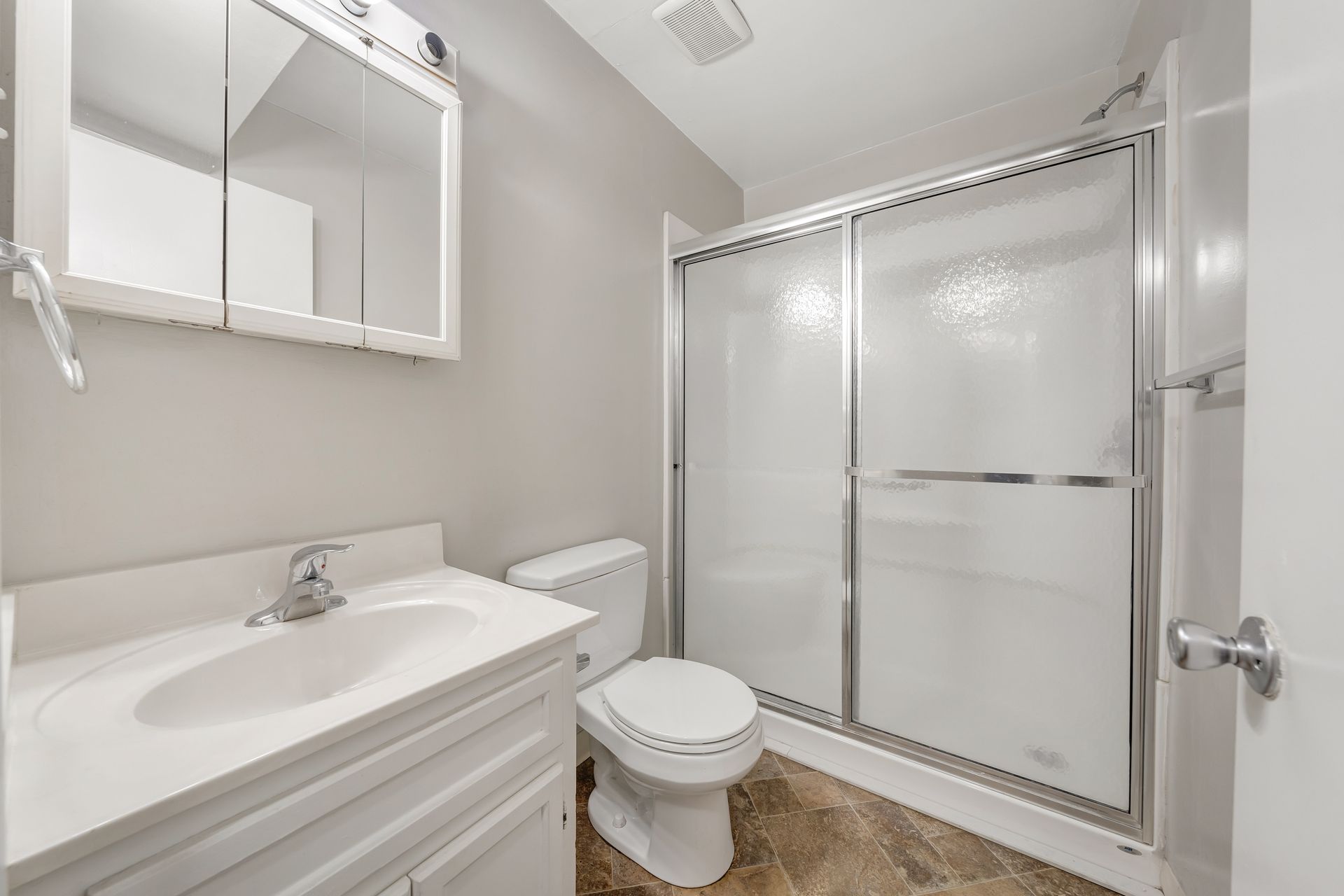 A bathroom with a toilet , sink , mirror and shower stall.