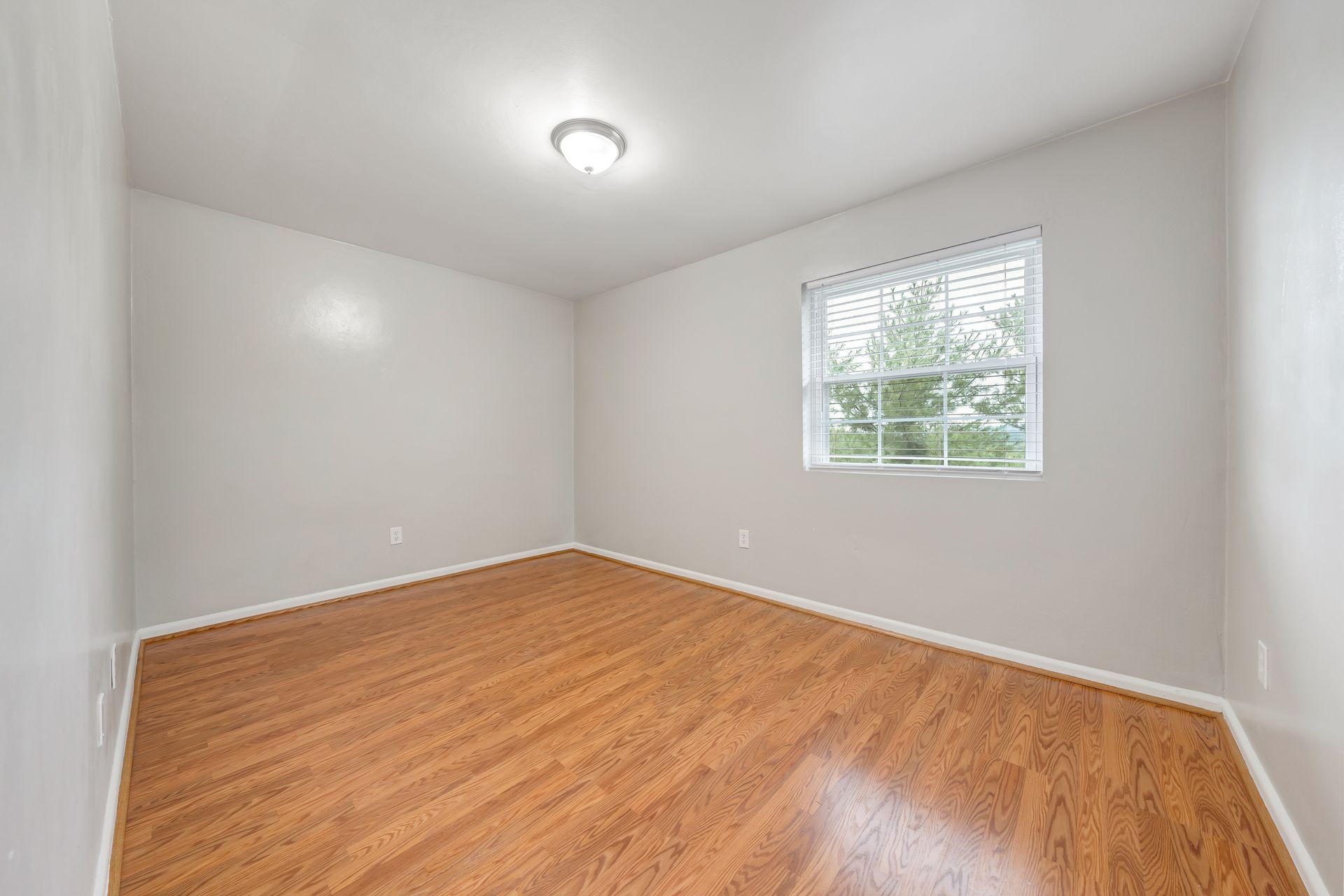 An empty bedroom with hardwood floors and a window.