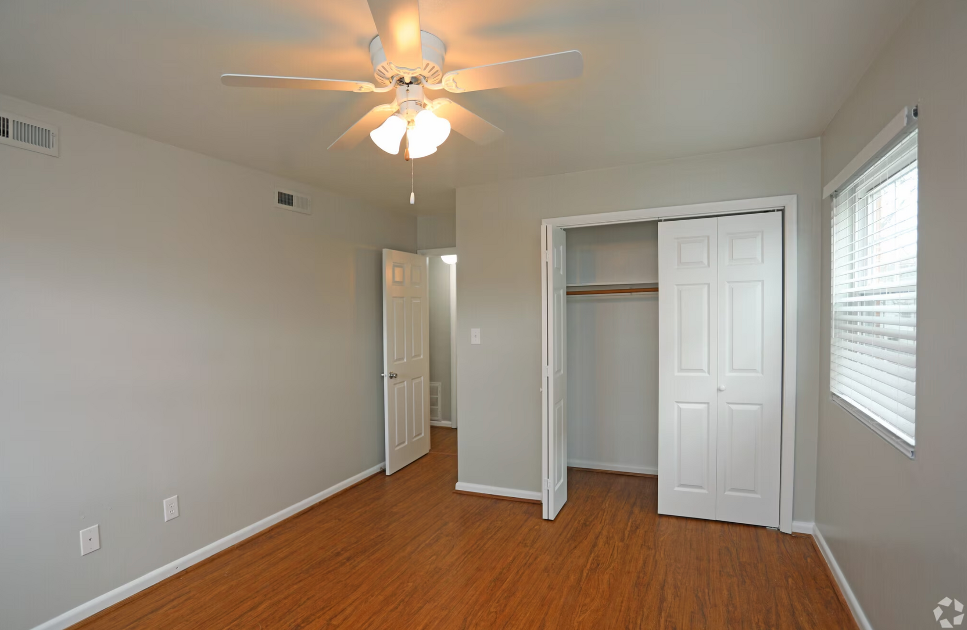An empty bedroom with hardwood floors and a ceiling fan.