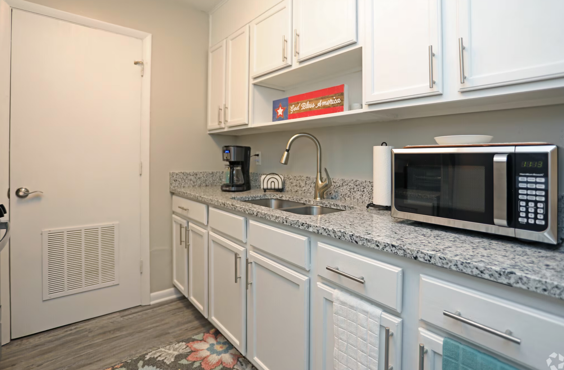 A kitchen with white cabinets , granite counter tops , a microwave and a sink.