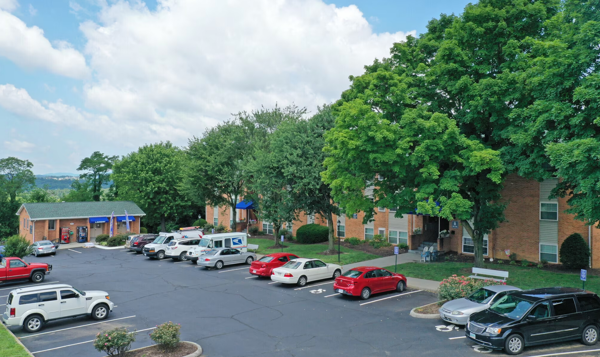 A row of cars are parked in a parking lot in front of a building.