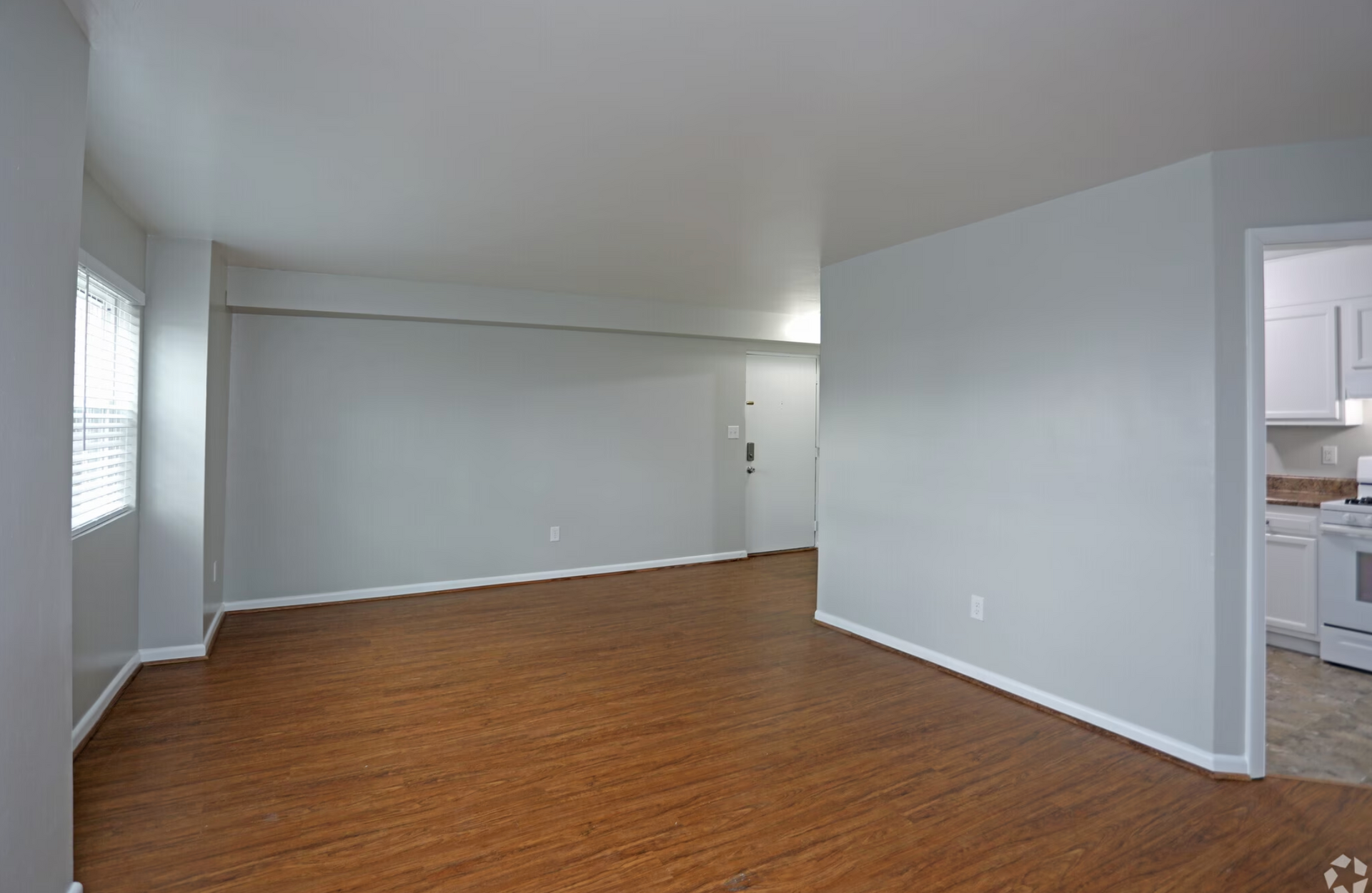 An empty living room with hardwood floors and white walls.