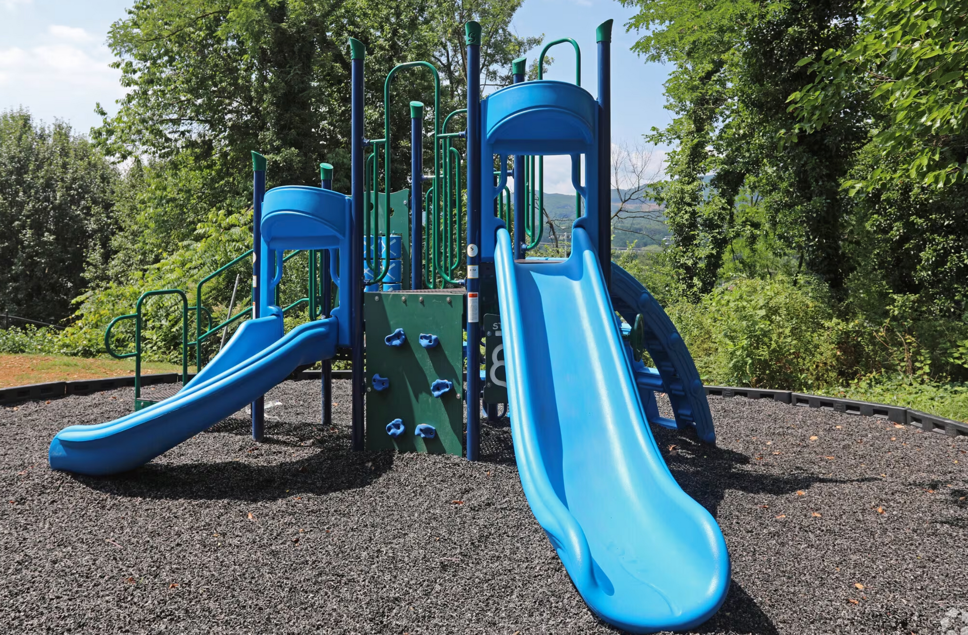 A blue and green playground with trees in the background.