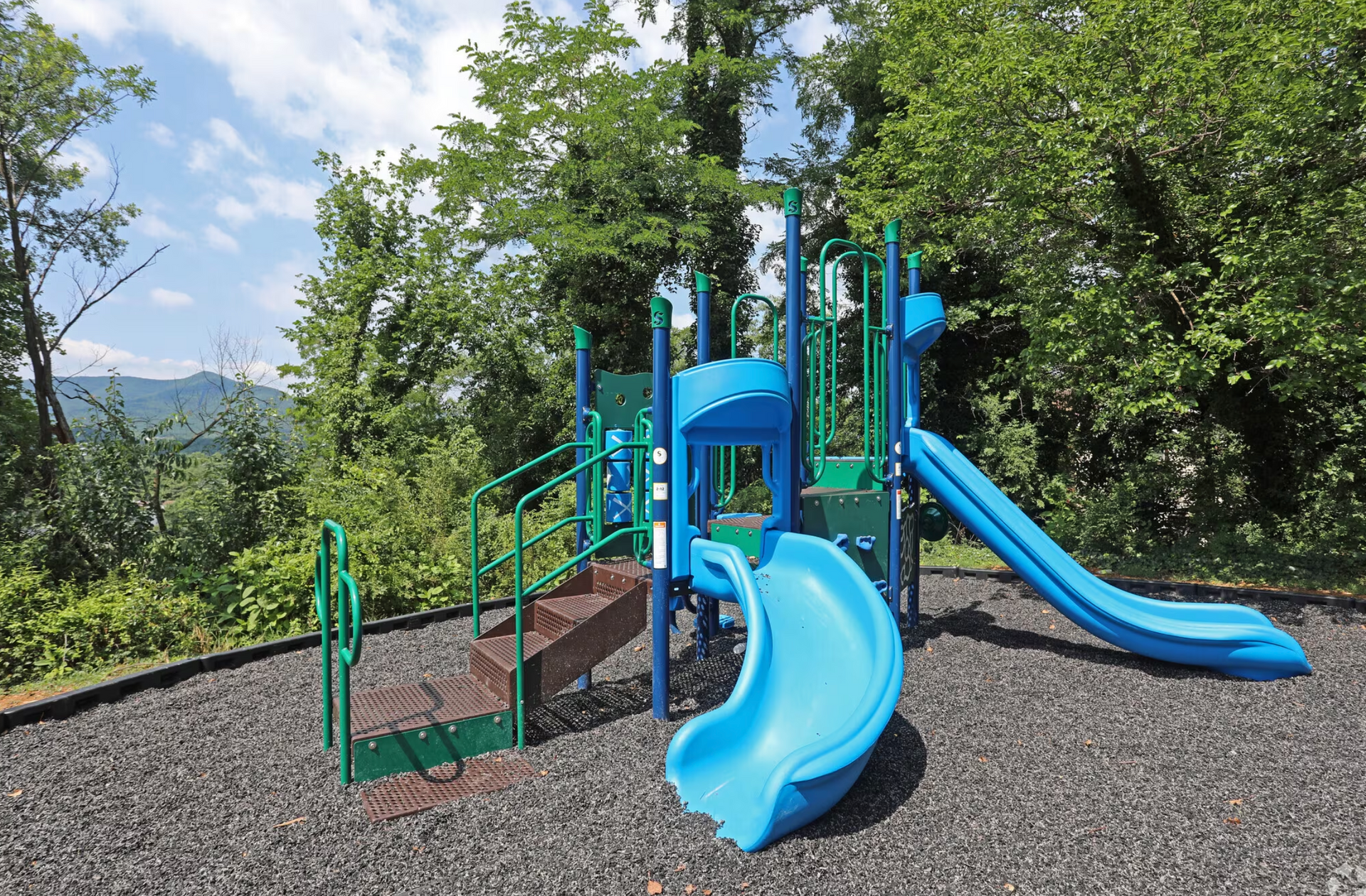 A blue and green playground with trees in the background.