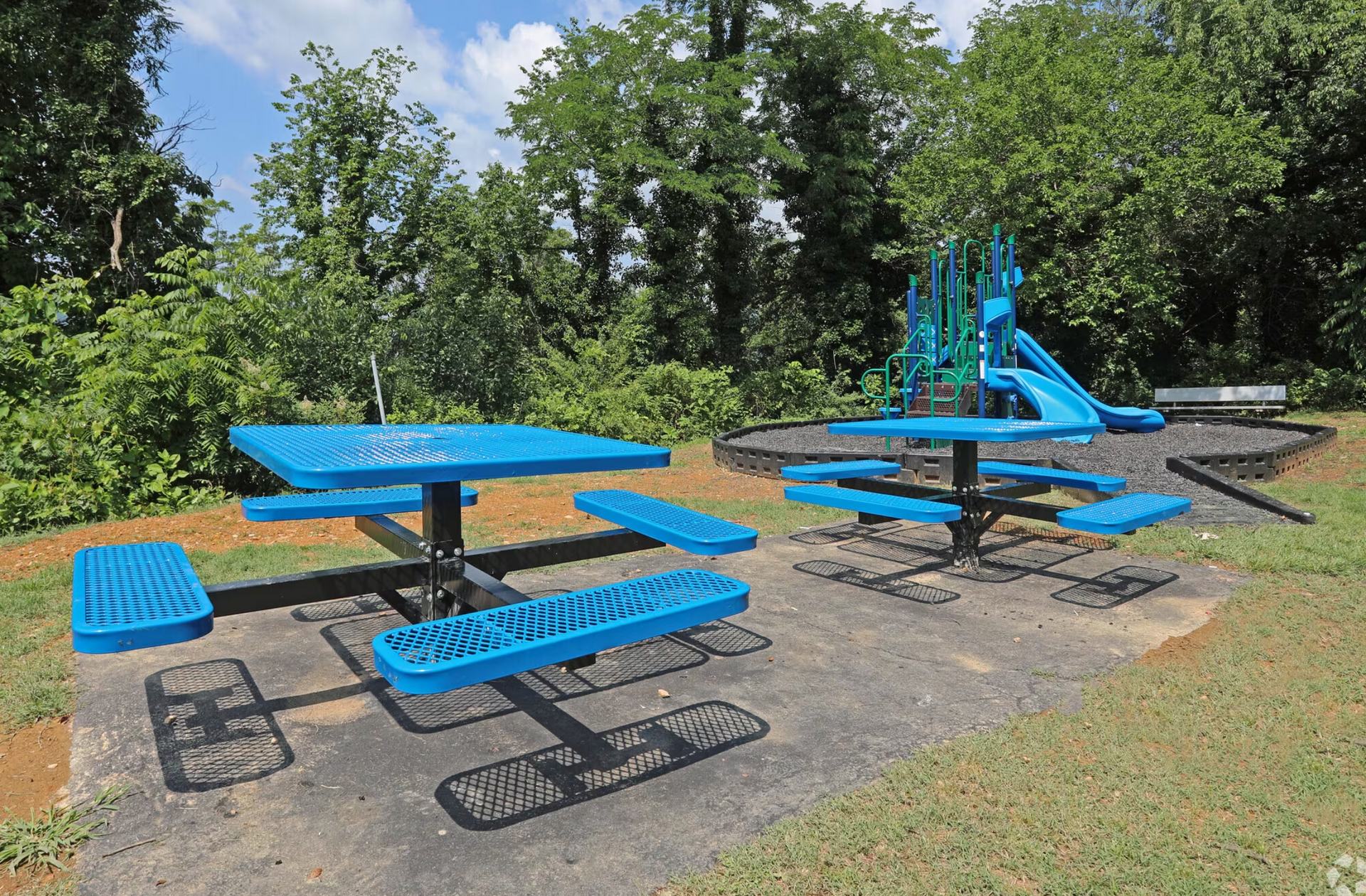 A blue picnic table in a park with a slide in the background.