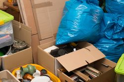 Boxes and blue garbage bags packed with household clutter in a storage area
