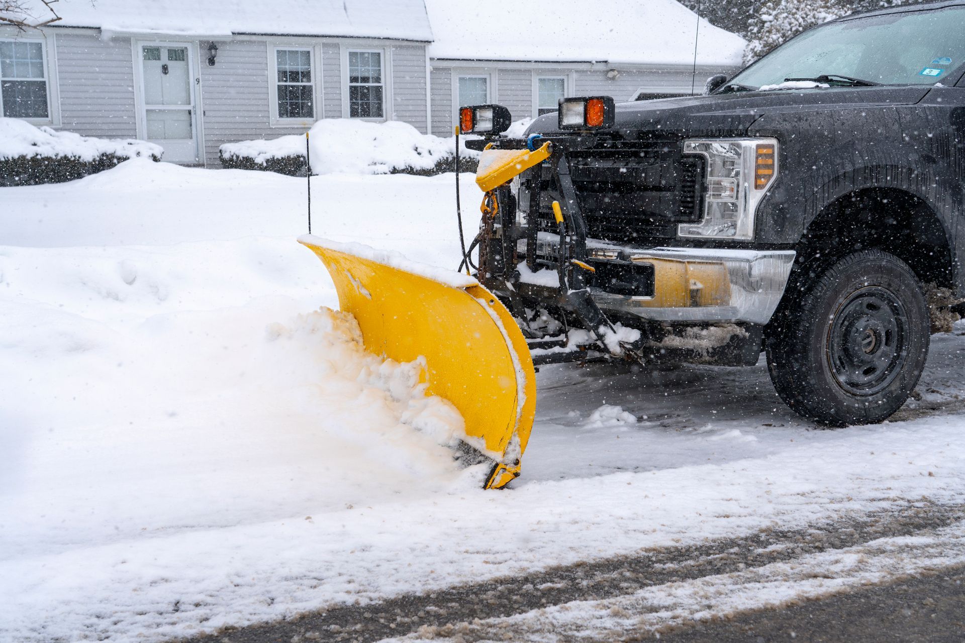 Yellow snowplow pushing snow on a residential street in winter