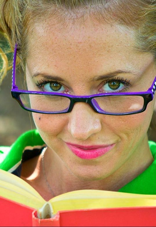 A woman wearing purple glasses is reading a book