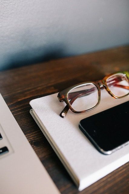 A pair of glasses sitting on top of a notebook next to a cell phone