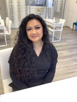 A woman with long curly hair is sitting at a table in a room.